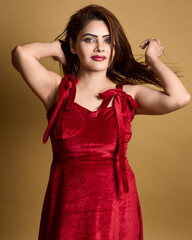 High-quality studio portrait of a fashionable woman in a red velvet dress styling her hair and looking confidently at the camera. Ideal for beauty, fashion, lifestyle, and empowerment themes.