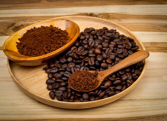 Whole coffee beans and ground instant coffee powder displayed on a round wooden plate and a spoon, ready for brewing.