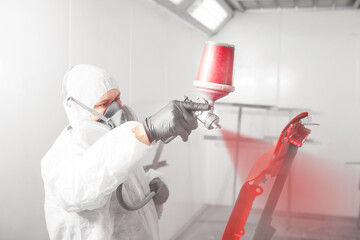 Male worker painting a fender of car in a white paint booth.