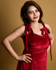 High-quality studio portrait of a fashionable woman wearing a red velvet dress and posing confidently with her hands on her waist. Ideal for beauty, lifestyle, and empowerment themes.