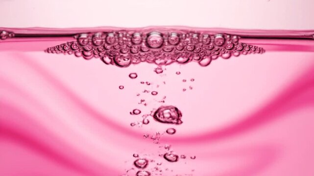 Pink liquid fills frame with bubble row atop and bubbles falling below
