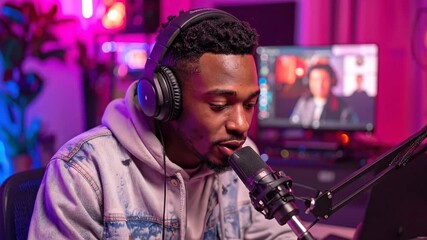 Energetic young man in a home studio, focused on recording a podcast or hosting a live online interview, with a vibrant purple and pink light setup in the background