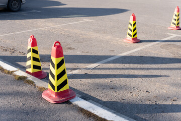 Several red and yellow striped traffic cones are arranged in an empty parking lot. The cones are...