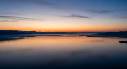 Obraz premium Serene lake at sunrise with misty mountains and orange sky