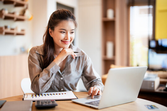 Happy asian business woman using laptop computer typing And working online sitting at home wearing casual. Office worker lady browsing internet on computer. Entrepreneurship.
