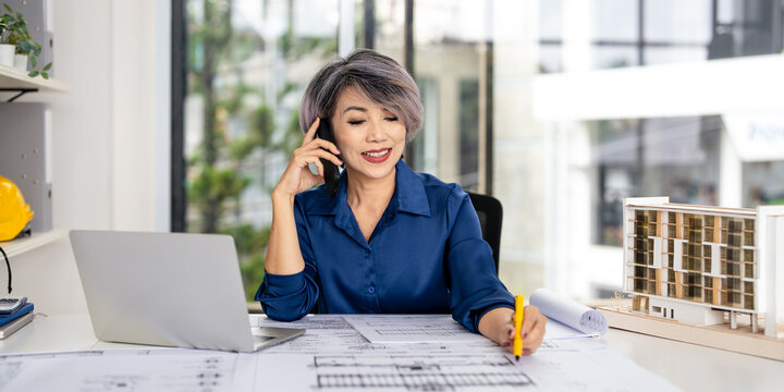 Professional civil engineer in construction site office. Talking on phone call working on shop drawings of post tension slab plan on desk.