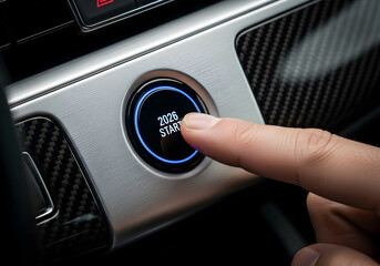 Close-up of a hand pressing a glowing car start/stop button labeled "2026 start" on a modern dashboard with carbon fiber accents