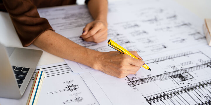 Close up hand of Architect or engineer hand holding pen working on blueprint floor plans  with  a pencil,  a ruler, calculator, smartphone, laptop and engineering tools.