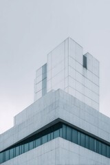Fototapeta premium A minimalist photograph of a modern building's upper section, showcasing clean lines, concrete textures, and a muted color palette against a pale sky