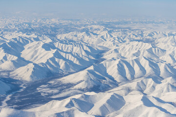 Aerial view of snow-capped mountains. Winter snowy mountain landscape. Air travel to the far North of Russia. Kolyma Mountains, Magadan Region, Siberia, Russian Far East. Great for the background.