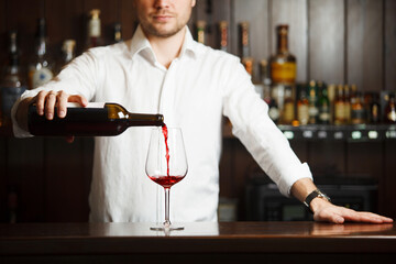 Male sommelier pouring red wine into long-stemmed wineglasses.