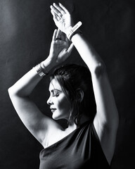 Monochrome portrait of an elegant woman captured in graceful motion with raised arms. Fine-art style lighting highlights emotion, beauty, and artistic expression. Perfect for fashion and conceptual