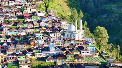 Aerial view of colorful hillside village with dense houses and a mosque surrounded by green mountains. Scenic rural architecture and landscape. Nepal Van Java, Mount Sumbing, Indonesia. - Powered by Adobe