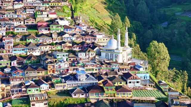 Aerial view of colorful hillside village with dense houses and a mosque surrounded by green mountains. Scenic rural architecture and landscape. Nepal Van Java, Mount Sumbing, Indonesia.