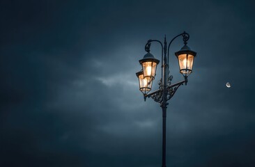A three-lamp ornate streetlight glows under a dark, moody sky, a sliver of moon visible in the upper right.  The lighting emphasizes the lamp's intricate details against the stormy clouds