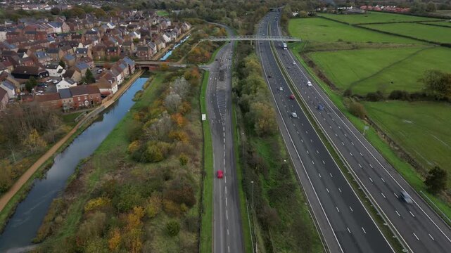 Dynamic drone video of M271 highway stretching through Southampton near Redbridge. Captures movement of vehicles, suburban homes, lush greenery, and autumn colors from above. Crisp, clear visual.