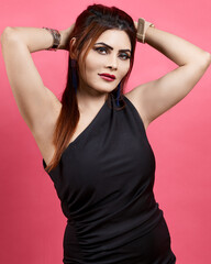 Fashion and beauty portrait of an elegant woman in a black dress posing confidently in studio light against a pink background. Represents style, grace, and empowerment.