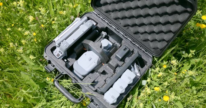 Open hard case with drone kit on a green meadow. Camera drone, controller and spare batteries arranged in foam
