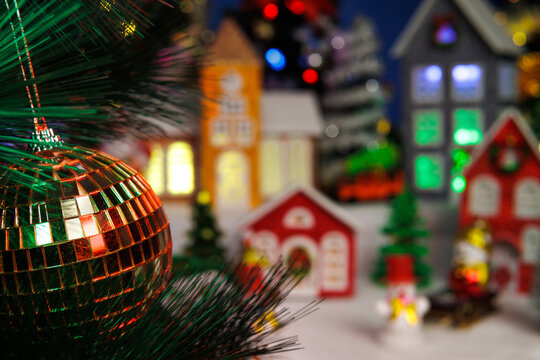 Behind the Christmas ball on the tree branch, a Christmas town is partially blurred