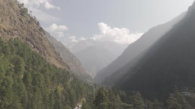 Aerial view of Parvati Valley near Chalal village showing rocky Himalayan mountains covered with pine and deodar trees on a cloudy autumn day, creating a dramatic, scenic Himachal landscape.