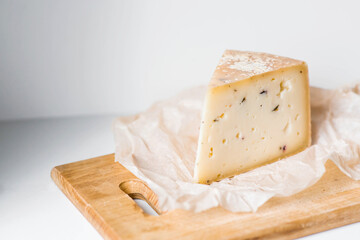 Quality of farm-fresh agricultural products. A piece of fresh, aged, natural farm cheese on parchment on a wooden board.
