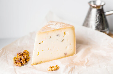 The quality of farm products is the freshness of agricultural products. A piece of fresh, aged, natural farm cheese with walnuts on parchment on a wooden board.