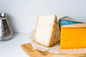 Unusual taste and quality of fresh farm products. Pieces of different fresh, aged, natural farm cheese in parchment paper on a wooden board.