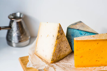 Unusual taste and quality of fresh farm products. Pieces of different fresh, aged, natural farm cheese in parchment paper on a wooden board.