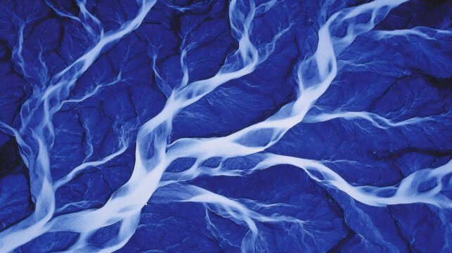 Aerial view of a braided river delta system in blue tones, forming abstract patterns across the Icelandic landscape