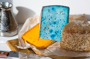 Unusual taste and quality of fresh farm products. Pieces of different fresh, aged, natural farm cheese in parchment paper on a wooden board.