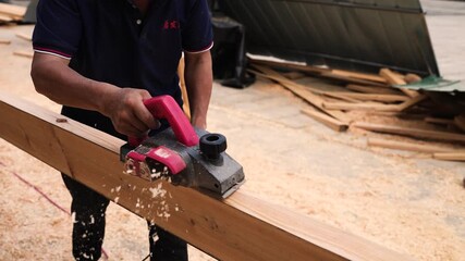 Carpenter Using Electric Hand Planer on Wood Beam