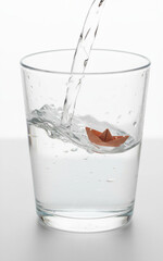 Pouring Water Inside a Glass with a Paper Boat Floating