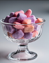 Pastel pink and purple candies in a clear glass dessert bowl on a light background.