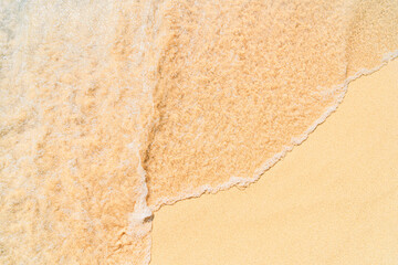 The image shows a close-up of sea foam rolling onto a sandy beach. The clear dividing line between the foam and the dry sand creates a minimalist and abstract visual effect.