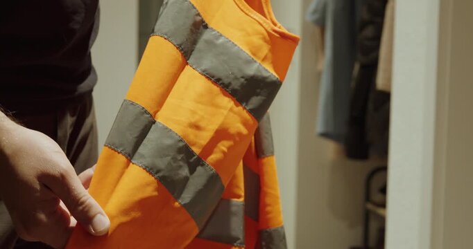 A man points to the reflective strips on his safety vest, demonstrating visibility, protection, and awareness for safety in dark work environments.
