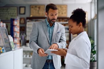 Mid adult man and his pharmacist using digital tablet in a pharmacy.