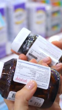 Close up of female hands holding two bottles of dietary supplements, carefully reading the nutritional information and ingredients on the label before purchasing in a pharmacy or store