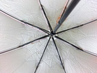 The intricate underside of an open umbrella, revealing its radial spokes and slightly wrinkled white fabric with faint pink hints.