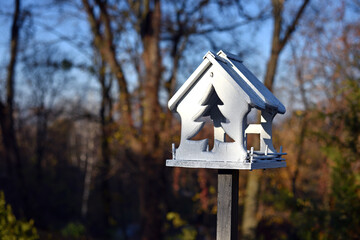 Wooden bird feeder with berries and wheat inside, birdhouse on a beautiful blurred background of yellow leaves outdoors. feeders in the autumn park. feed wild birds during the cold season. close-up