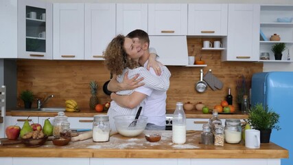 Joyful young couple wearing pajamas dancing and hugging romantically in the kitchen while preparing breakfast together, enjoying a happy morning and sharing a tender moment at home
