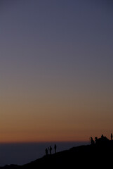 The photographers' silhouettes waiting to see the sunrise on the mountaintop in the early morning, and a sunrise scene (zoom shot) / 早朝の山頂で御来光の瞬間を待つカメラマンたちのシルエットと朝焼けシーン(冬の朝，望遠ズーム撮影)