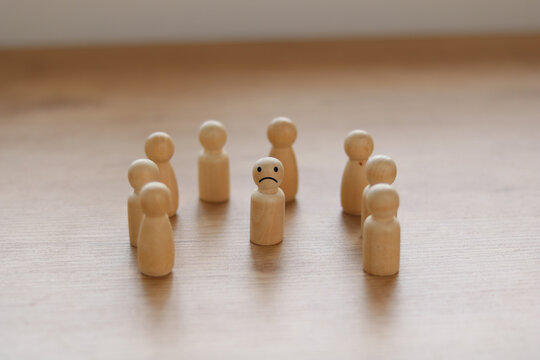 Wooden figures arranged in a circle with one sad figure in the center. Concept of loneliness, social isolation, bullying, depression, mental health, or feeling excluded from a group.