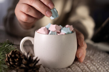closeup hand placing pastel marshmallow, home barista arranging garnish on cocoa, pinecone and evergreen