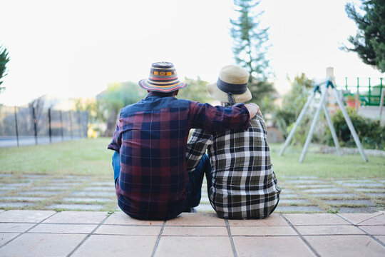 Elderly couple sitting together on a tiled patio, embracing and looking out at the grassy backyard, sharing a moment of retired life and companionship