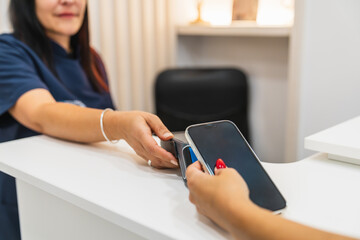 Woman making contactless mobile payment using a smartphone at a reception desk in a physiotherapy, cosmetics, or aesthetics clinic