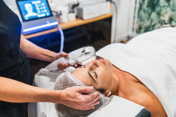 Woman having high intensity focused ultrasound facial treatment for skin tightening and anti aging in a beauty clinic