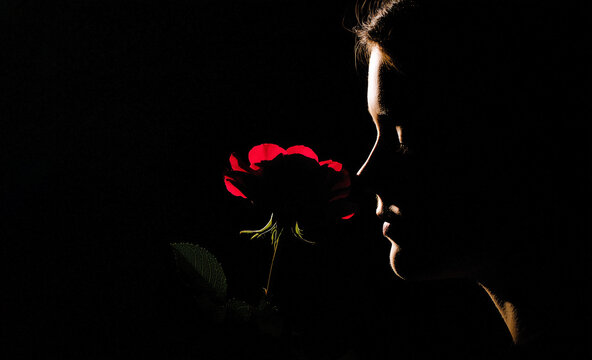 Beautiful young  woman with a red rose on a black background. Copy space