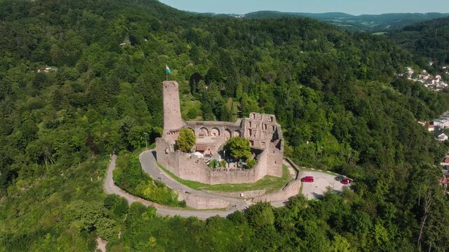 Aerial drone orbiting around the ruins of Dilsberg Castle near Heidelberg, Germany, surrounded by forested hills and a winding road leading to the site.