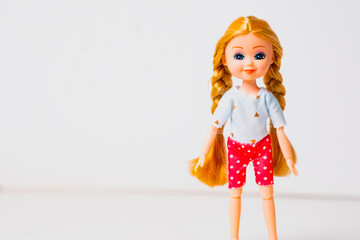 A cheerful toy doll with long blonde hair is dressed in a light blue top and red polka-dotted shorts. The doll stands upright, showcasing its vibrant appearance against a simple backdrop. © Anton Dios