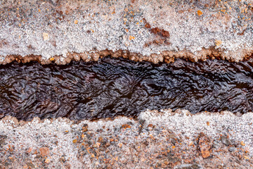 Maras, Cusco, Peru: close-up of the mineral water canal feeding the salt terraces. Natural salt crystals forming along the edge of the dark stream in the Sacred Valley of the Incas.